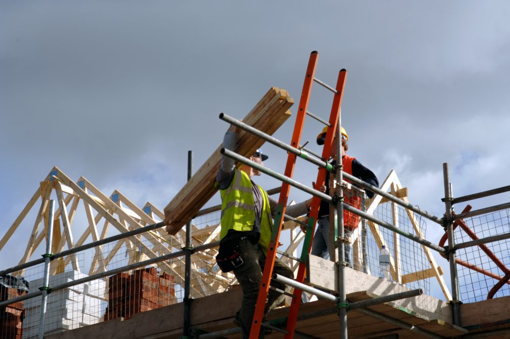 Low view of two construction workers on top of house frame