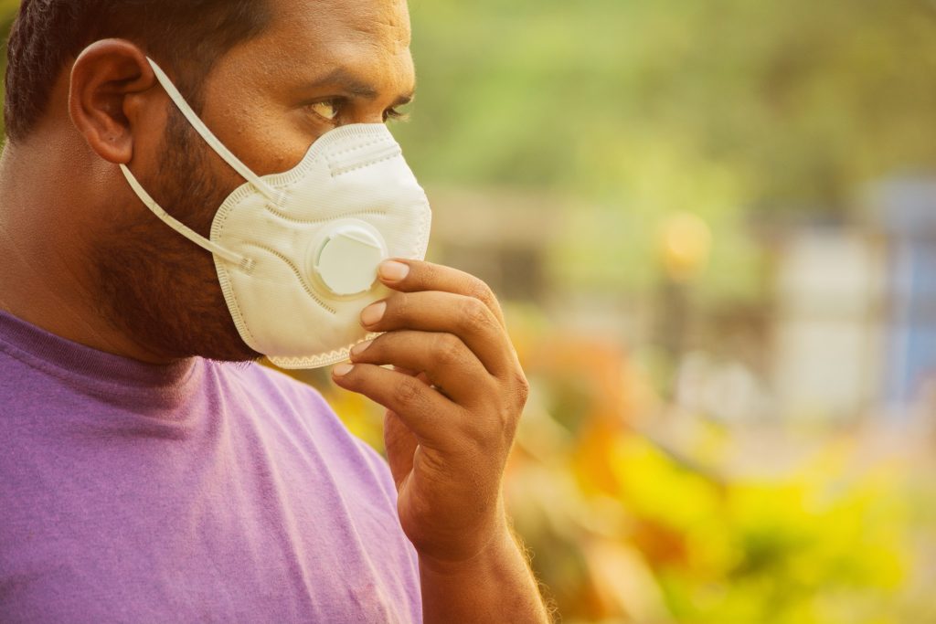 Worker wearing a disposable respirator mask outdoors, adjusting the fit to protect against airborne contaminants, supporting the topic “Clear Air, Clear Benefits: Air Quality Monitoring as Part of Your Occupational Hygiene Strategy”, highlighting the importance of air quality monitoring, exposure control, and respiratory protection in occupational hygiene to manage dust, particulates, and harmful airborne substances in workplace environments and maintain compliance with UK health and safety standards