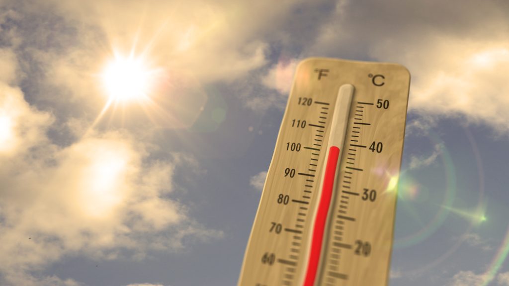 Outdoor thermometer showing a temperature of approximately 40°C beneath intense summer sunlight and a partly cloudy sky, illustrating how hot weather can affect workplace conditions and alter employee exposure to airborne dust, fumes and vapours.